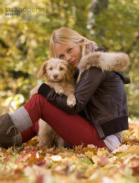 Österreich  Junge Frau sitzend mit Hund auf Herbstblatt  lächelnd  Portrait