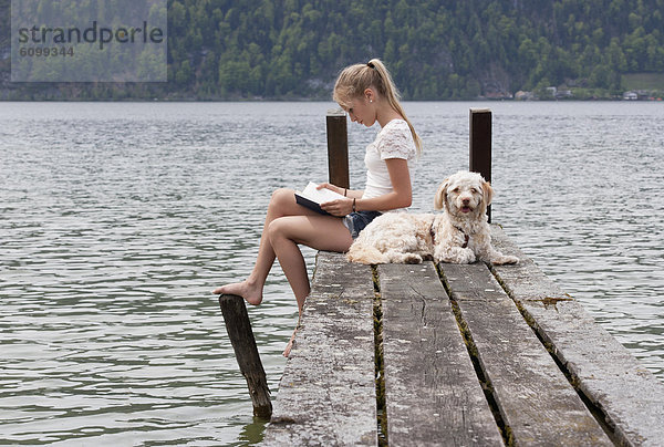 Österreich  Teenagermädchen Lesebuch neben Hund am Steg