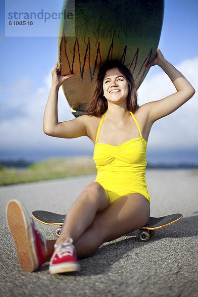 sitzend  Helligkeit  Frau  lächeln  Badeanzug  gelb  über  halten  Surfboard  Fernverkehrsstraße  Skateboard  jung  Kleidung