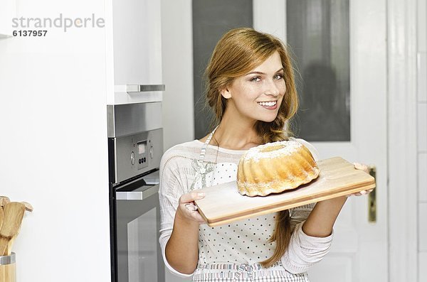Lächelnde junge Frau mit einem Kuchen in der Küche