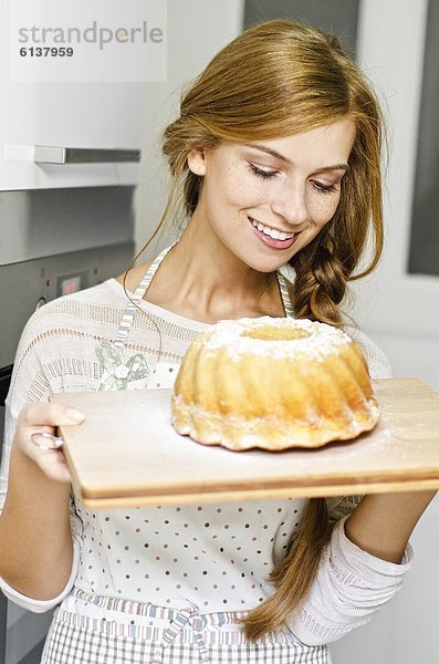 Lächelnde junge Frau mit einem Kuchen in der Küche