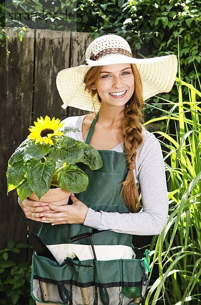 Lächelnde junge Frau mit einer Sonnenblume im Garten