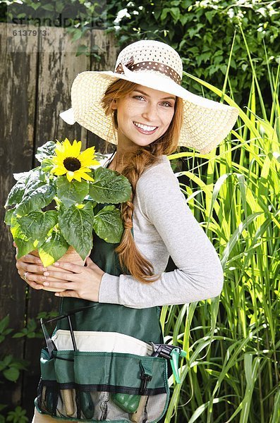 Lächelnde junge Frau mit einer Sonnenblume im Garten