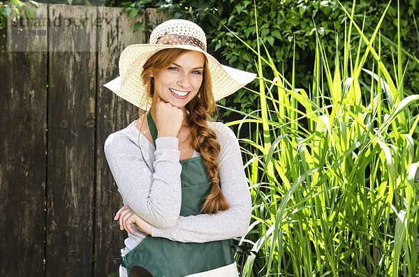 Lächelnde junge Frau mit Sonnenhut und Schürze im Garten