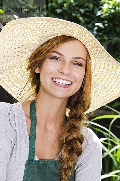 Lächelnde junge Frau mit Sonnenhut und Schürze im Garten  Portrait