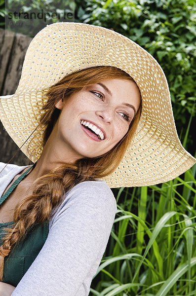 Lächelnde junge Frau mit Sonnenhut und Schürze im Garten