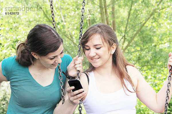 Teenager-Mädchen mit Handy auf Schaukeln