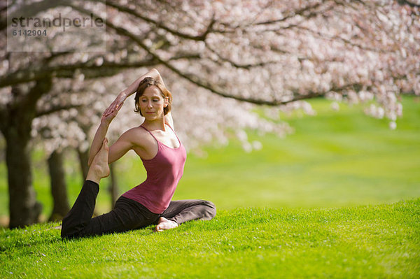 Frau in Tauben-Yoga-Pose unter Kirschbaum