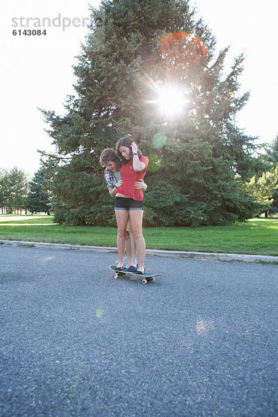 Teenager-Junge hilft Freundin beim Skateboardfahren