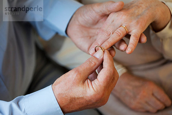 Senior Mann  der den Ehering auf den Finger der Seniorin legt.