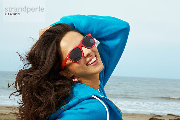 Junge Frau am Strand mit Hand im Haar und roter Sonnenbrille