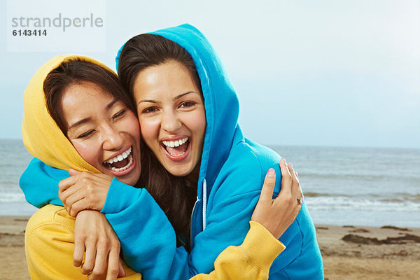 Zwei junge Frauen in Kapuzenoberteilen am Strand