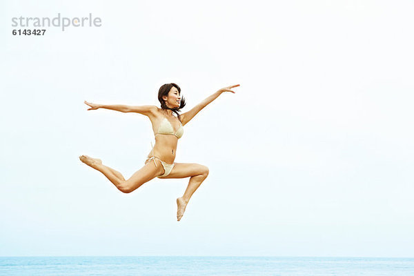 Junge Frau im Bikini beim Springen am Strand