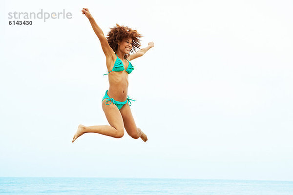 Junge Frau im türkisfarbenen Bikini am Strand springen