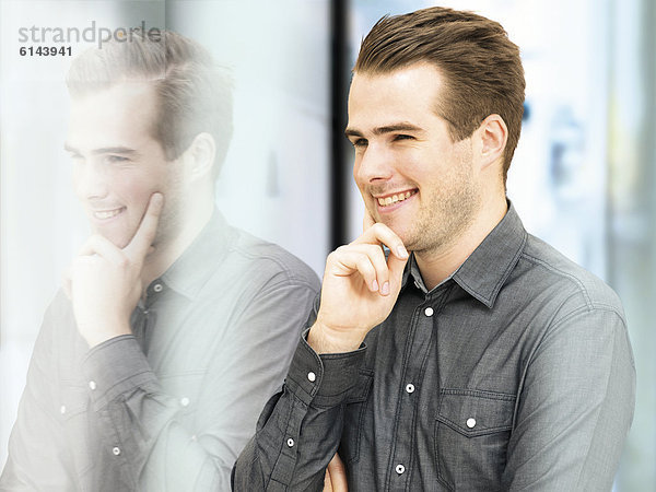 Lächelnder junger Geschäftsmann vor Glasscheibe mit Spiegelbild
