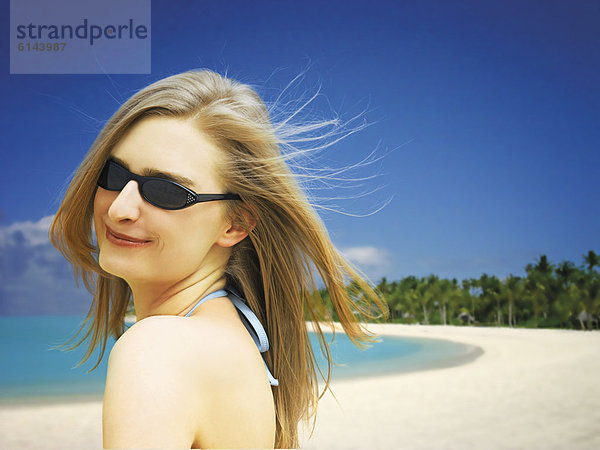Lächelnde  junge Frau mit Sonnenbrille und Bikini am Strand auf den Malediven