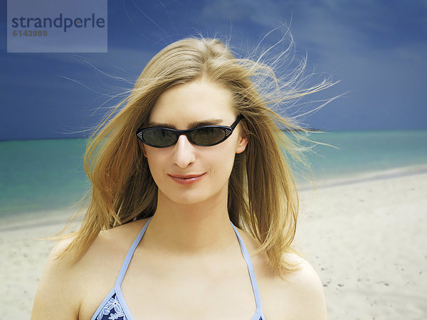 Lächelnde  junge Frau mit Sonnenbrille und Bikini am Strand auf den Malediven