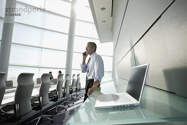 Geschäftsmann mit Handy schaut aus dem Fenster eines Konferenzraumes