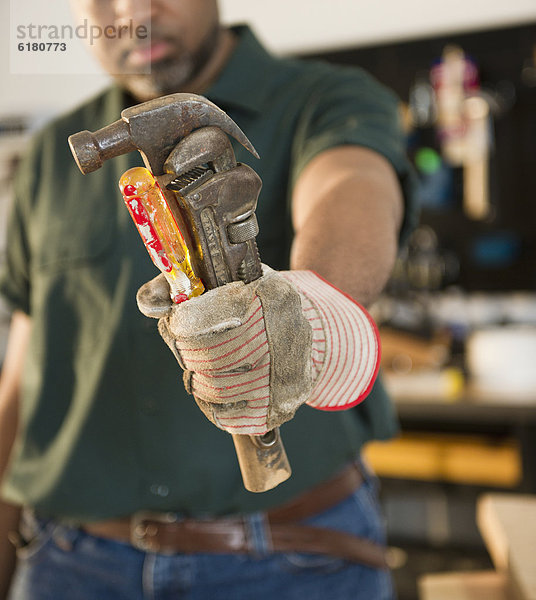 African American carpenter holding screwdriver  wrench and hammer