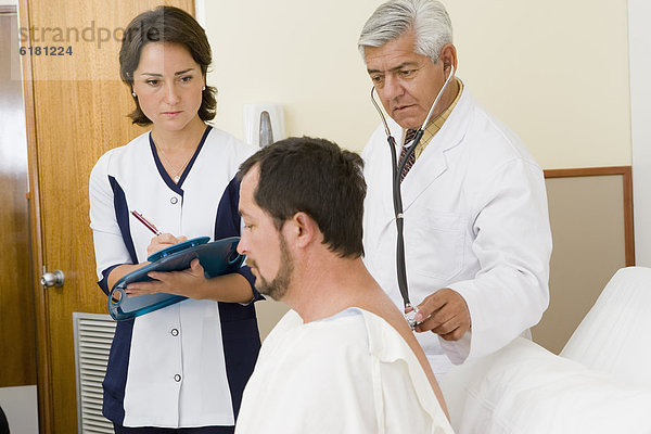 Arzt und Krankenschwester untersucht Patient im Krankenhauszimmer