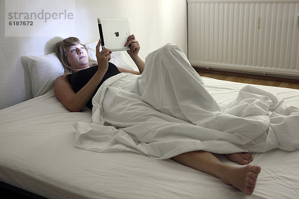 Junge Frau surft im Bett mit einem iPad  Tablet-Computer per Drahtlosverbindung im Internet