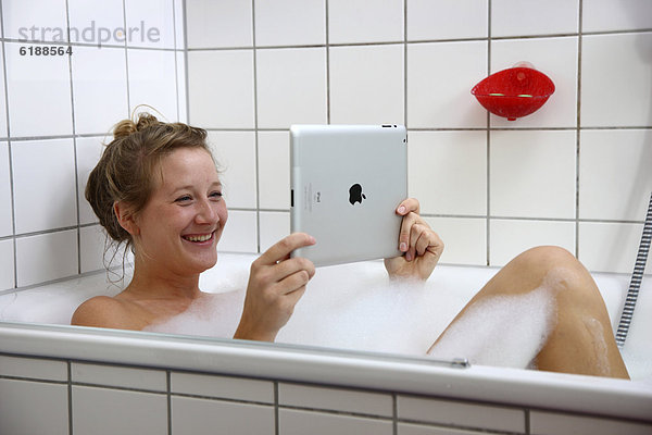Junge Frau in der Badewanne mit einem iPad  Tablet-Computer  drahtloser Internet-Zugang