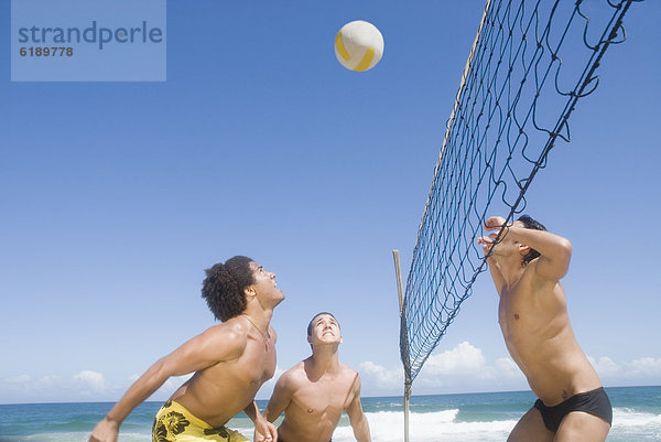 Drei Freunde spielen Beachvolleyball