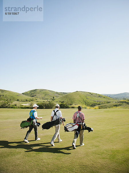 Männer tragen Golftaschen auf Golfplatz