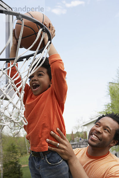 Menschlicher Vater  Sohn  heben  Basketball  einlochen