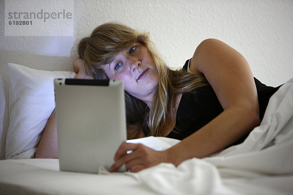 Junge Frau im Bett surft mit einem iPad  Tablet-Computer per Drahtlosverbindung im Internet