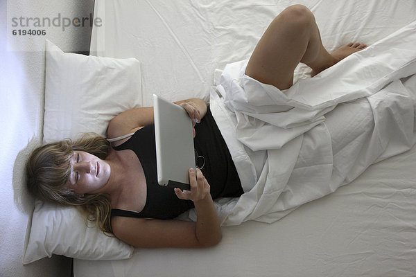 Junge Frau im Bett surft mit einem iPad  Tablet-Computer per Drahtlosverbindung im Internet