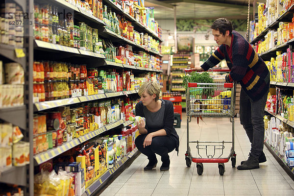 Junges Paar beim Einkauf zwischen Regalen mit diversen Lebensmitteln  Lebensmittelabteilung  Supermarkt  Deutschland  Europa