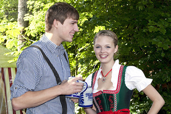 Junges Paar in Dirndl und Lederhose steht im Biergarten  bei Pettstatt  Oberfranken  Bayern  Deutschland  Europa