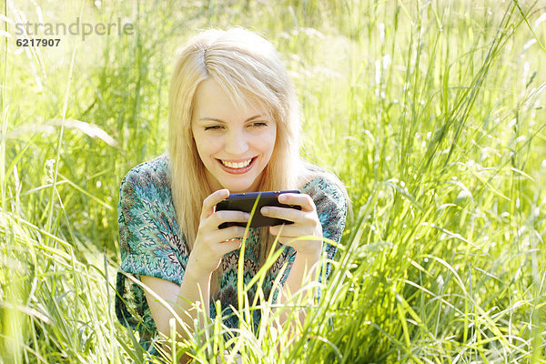 Junge Frau sitzt auf einer Wiese im hohen Gras und kommuniziert per Mobiltelefon