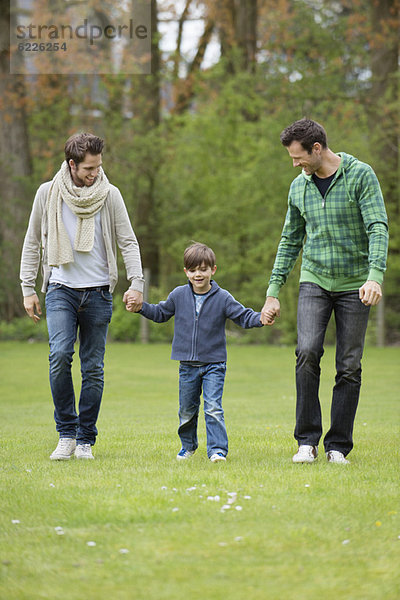 Junge  der mit zwei Männern in einem Park spazieren geht.