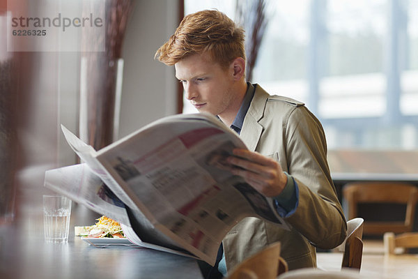 Ein Mann  der in einem Restaurant sitzt und eine Zeitung liest.