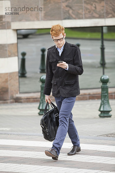 Geschäftsmann beim Überqueren einer Straße mit dem Handy