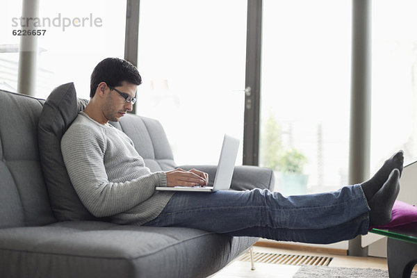 Mann mit einem Laptop auf einer Couch