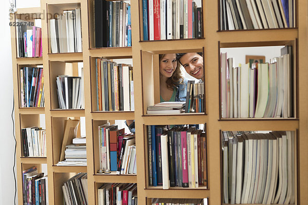 Ein Paar schaut aus einem Loch im Bücherregal.
