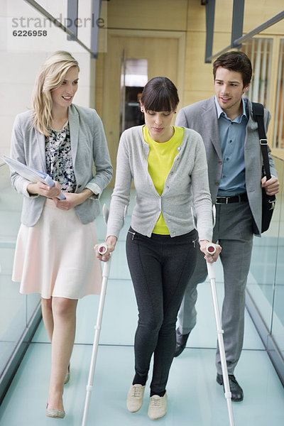 Behinderte Frau  die mit Geschäftsführern in einem Büroflur geht.