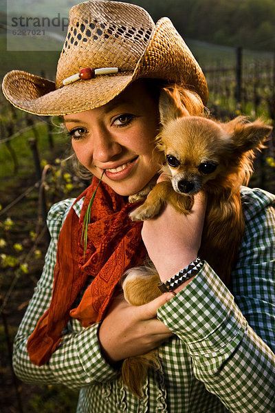 Lächelnde junge Frau mit Hut hält einen Hund  Portrait