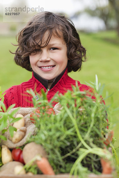 Glücklicher Junge mit einer Kiste einheimischen Gemüses
