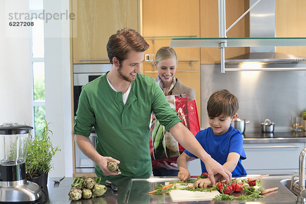 Eltern  die ihren Sohn beim Gemüseschneiden in der Küche anschauen