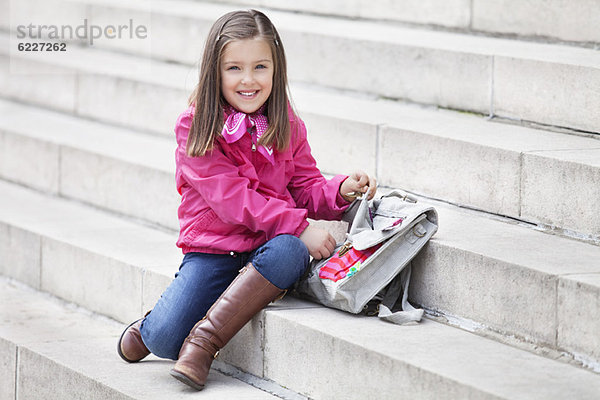 Porträt eines Mädchens  das seine Schultasche öffnet und lächelt