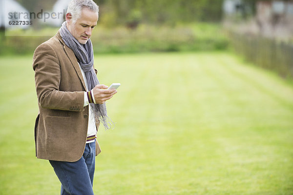 Man Textnachrichten auf einem Mobiltelefon in einem Park