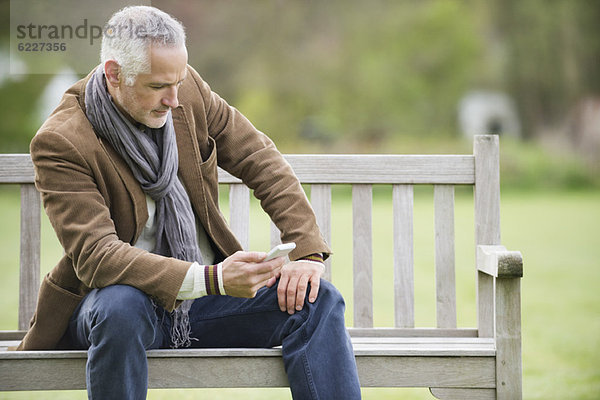 Man Textnachrichten auf einem Mobiltelefon in einem Park