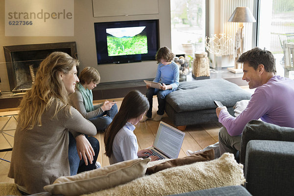 Familie mit elektronischen Geräten im Wohnzimmer