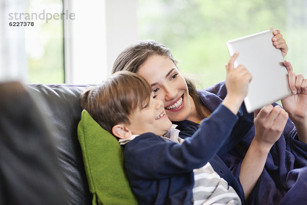 Frau mit ihrem Sohn auf ein digitales Tablett schauend und lächelnd