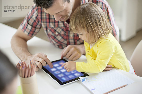 Mann  der seiner Tochter ein digitales Tablett beibringt.