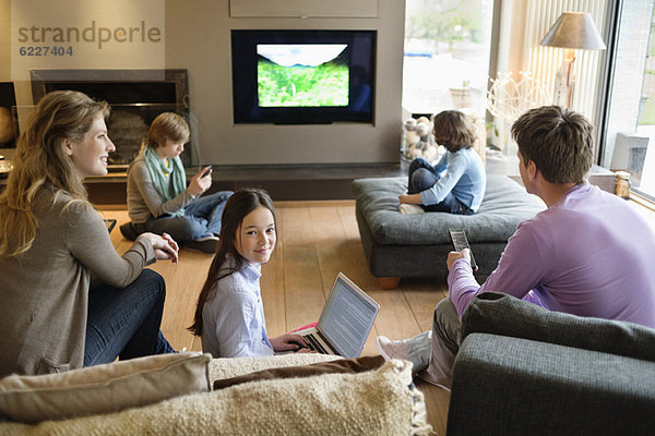 Familie mit elektronischen Geräten im Wohnzimmer